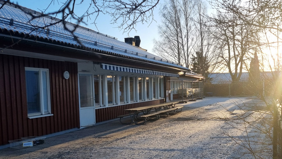 Röd förskolebyggnad med snö på taket i vintersol.