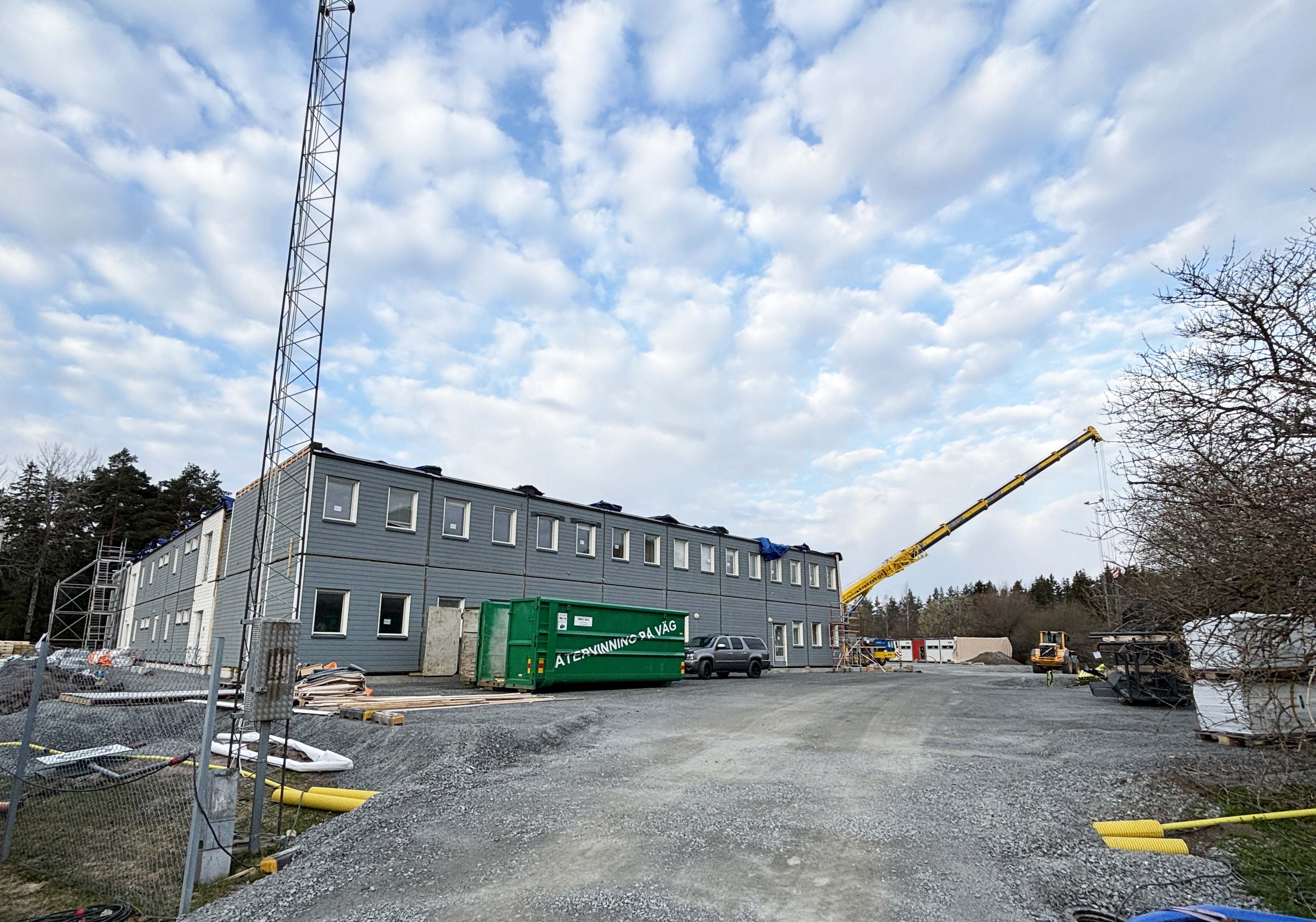 Byggnation av en modulskola på en grusyta med gul lyftkran i bakgrunden.