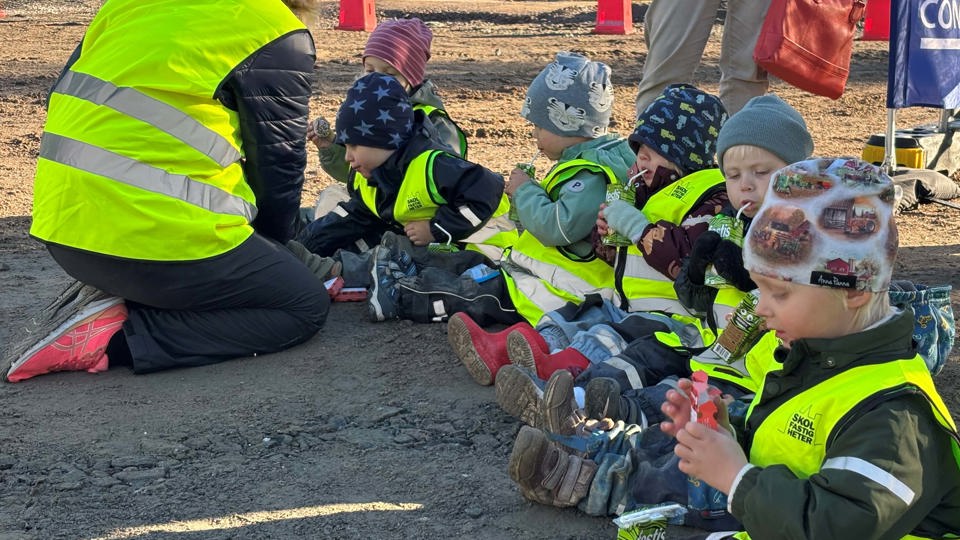 Barn med gula byggvästar fikar på en byggplats.