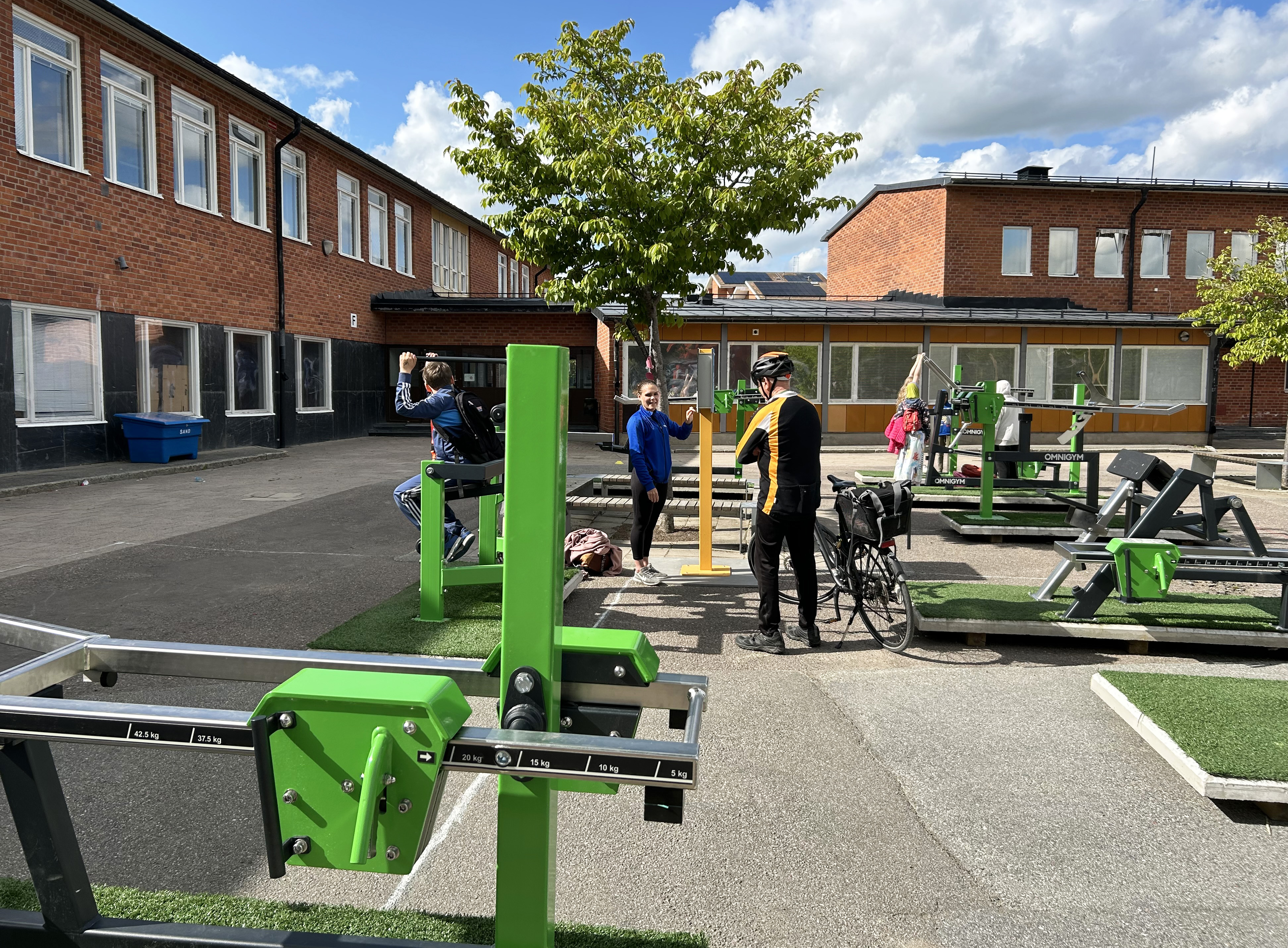 Skolgård med utegym där barn och äldre tränar.