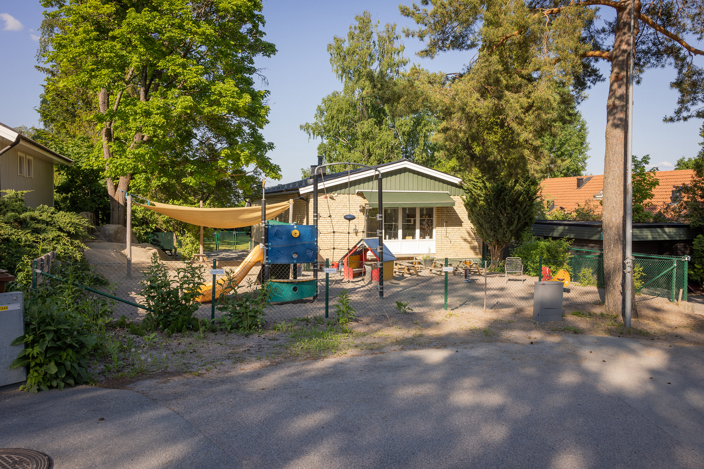 Gul tegelförskola med gård, klätterställning och lekutrustning i förgrunden.