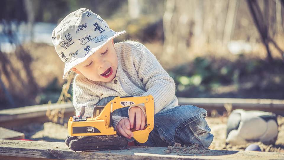 En liten förskolepojke leker med en gul grävmaskin i en sandlåda