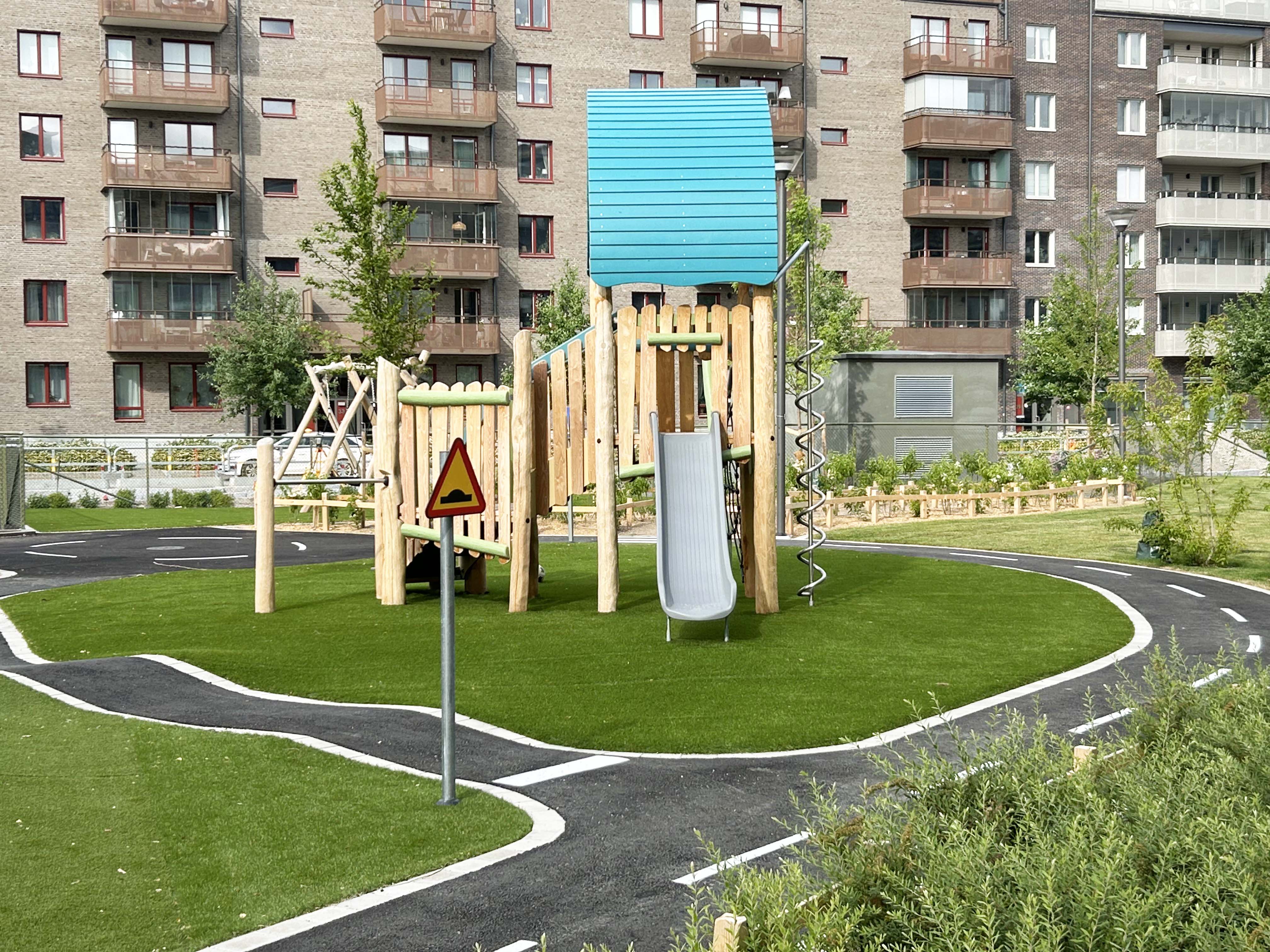 Ny förskolegård med lekutrustning i trä, gröna planteringar och lekväg.