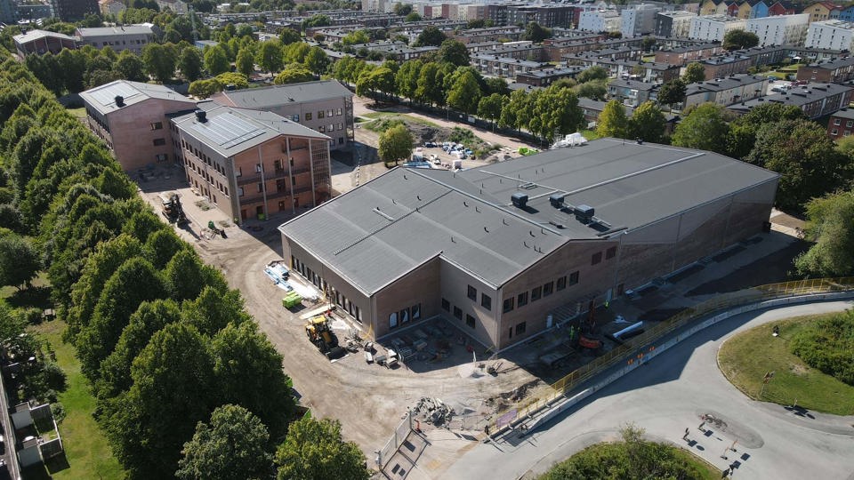 Flygfoto över byggplats där skola med skolgård och gröna träd växer fram.