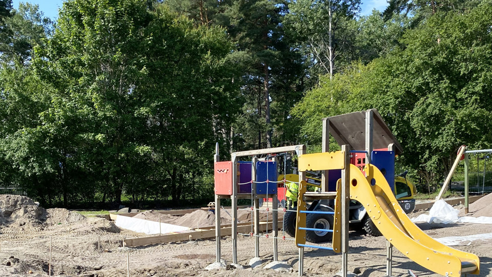 Byggarbetsplats på förskolegård, med klätterställning i förgrunden och skog i bakgrunden. 