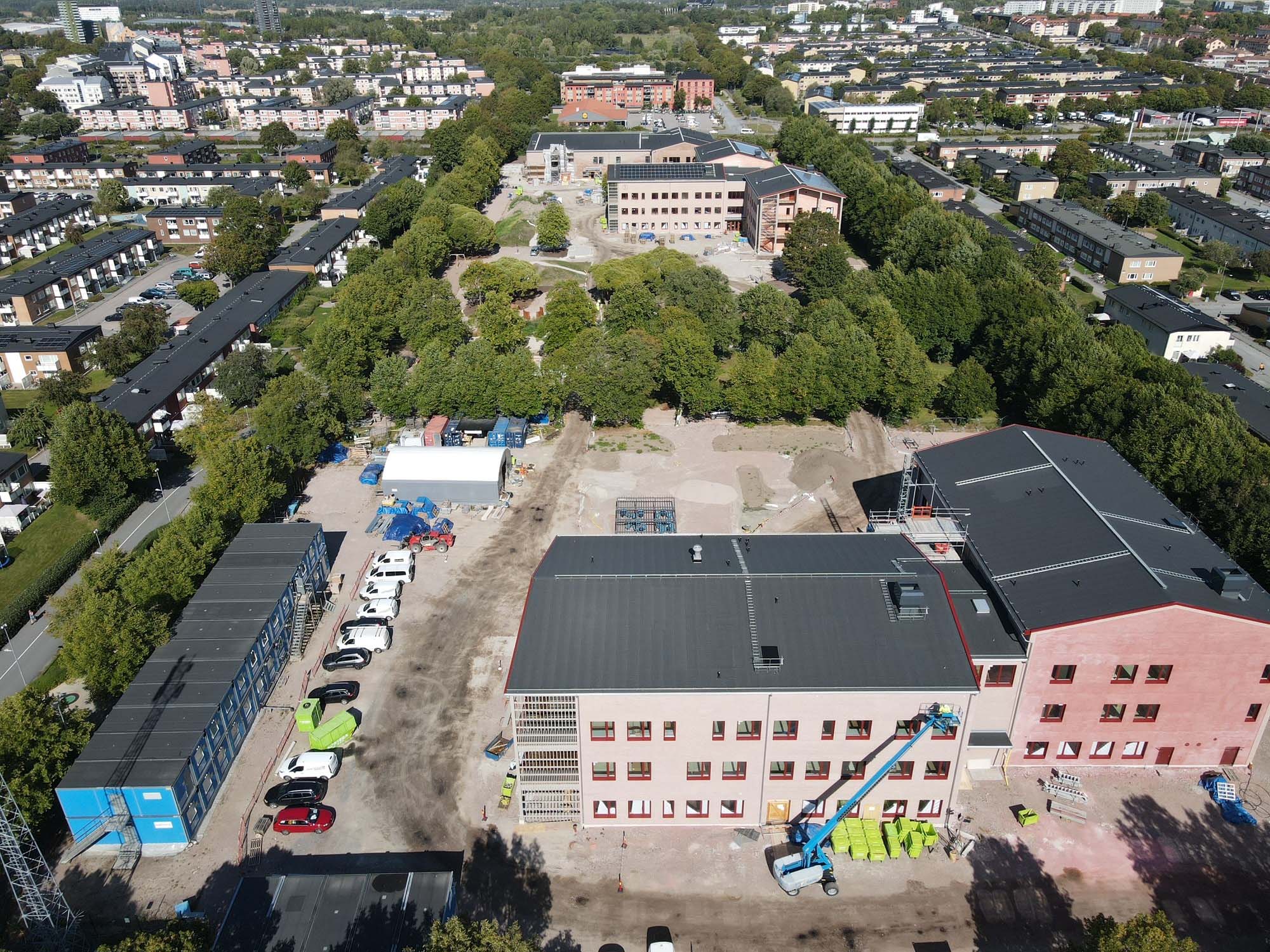 Flygfoto över byggplats där skola med skolgård och gröna träd växer fram .