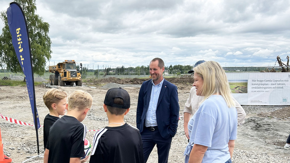 Fotbollsungdomar som pratar med vuxna på en byggplats där en ny plan ska byggas.