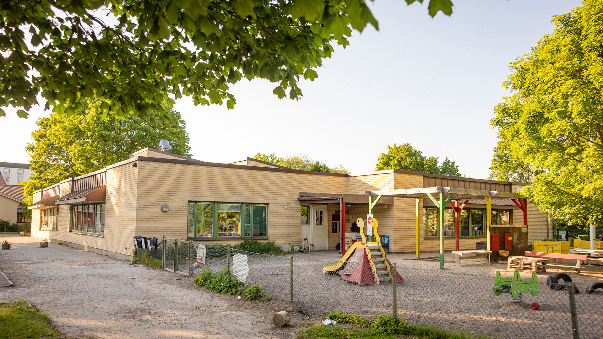 Förskola i gult tegel med skolgård, grusplan och lekutrustning