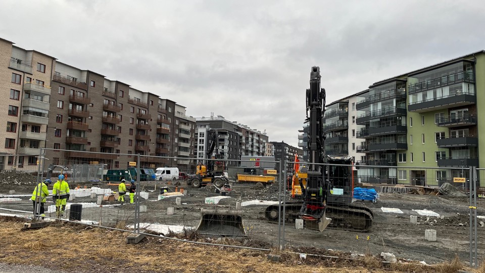 Grävmaskin arbetar på byggplats med byggarbetare i förgrunden