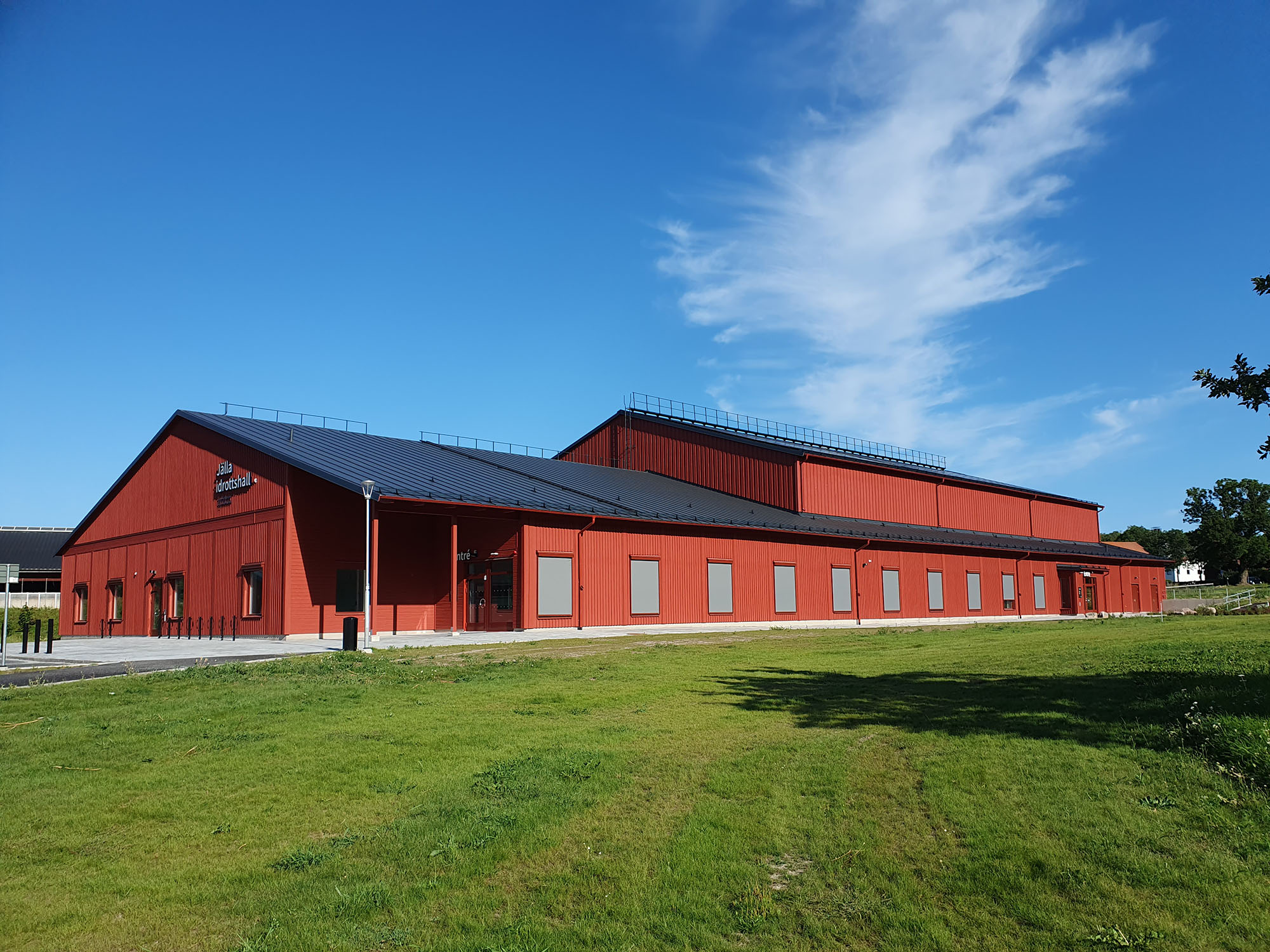 Röd nybyggd idrottshall i trä med en grön gräsmatta i förgrunden
