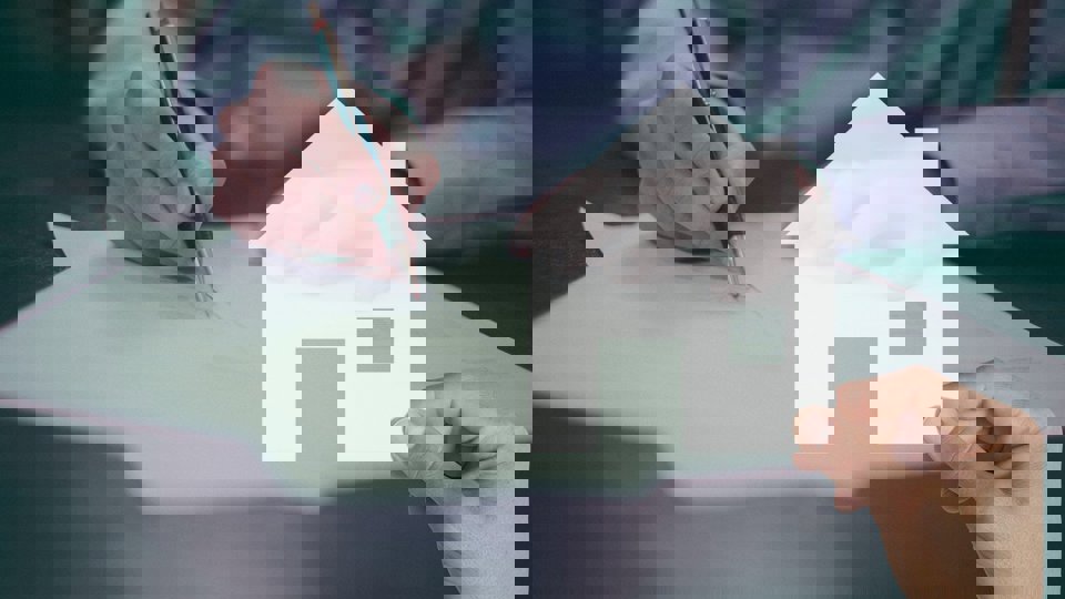 Hand som skriver på papper bakom symbolbild av ett hus