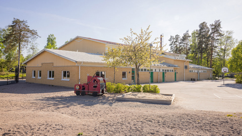 Gul tegelbyggnad med grusyta vid Järlåsa skola