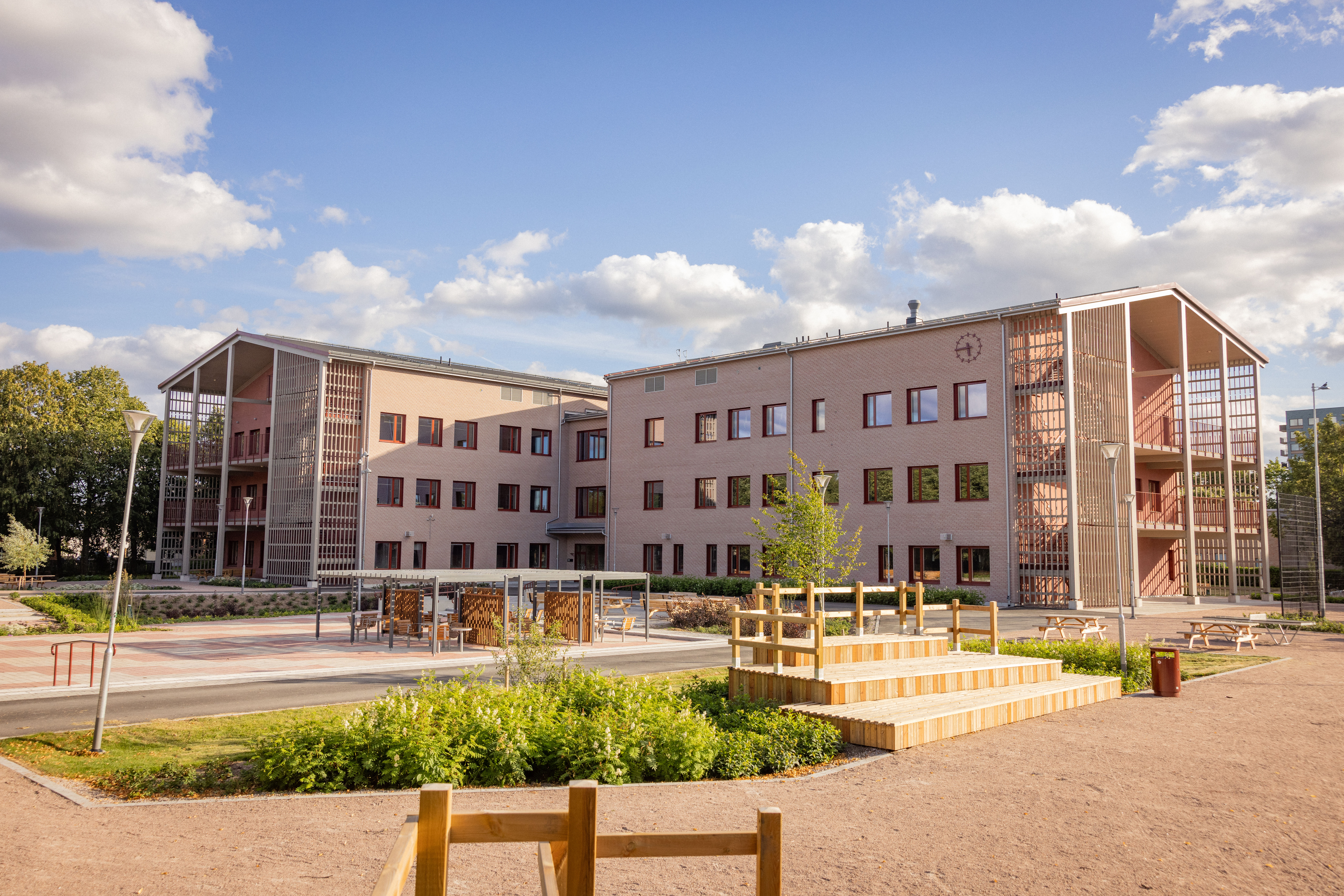 Nya skola med utemiljö och träbänkar sedd på avstånd.