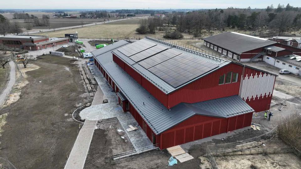 Röd byggnad belägen i lantlig lantbruksmiljö med fält och skog i bakgrunden.