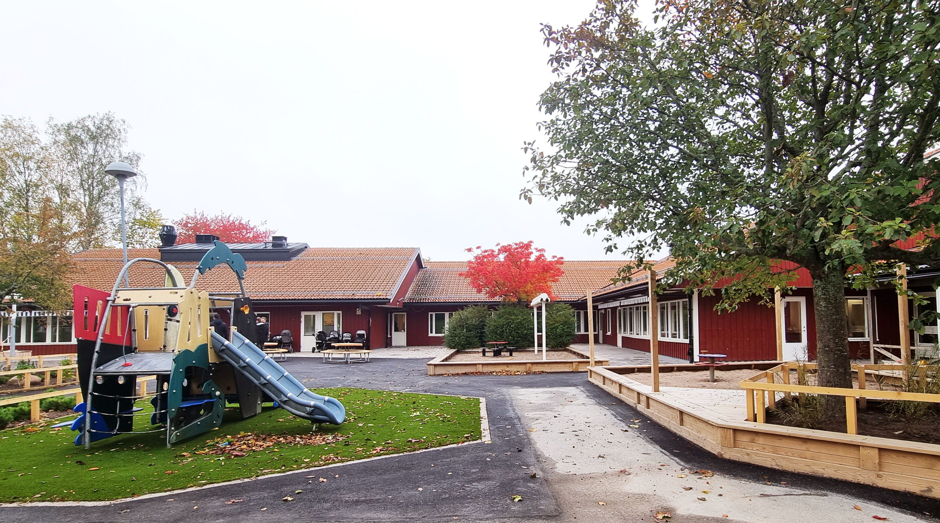 Nyrenoverad gård på en röd förskola med lekutrustning och nya träkonstruktioner.