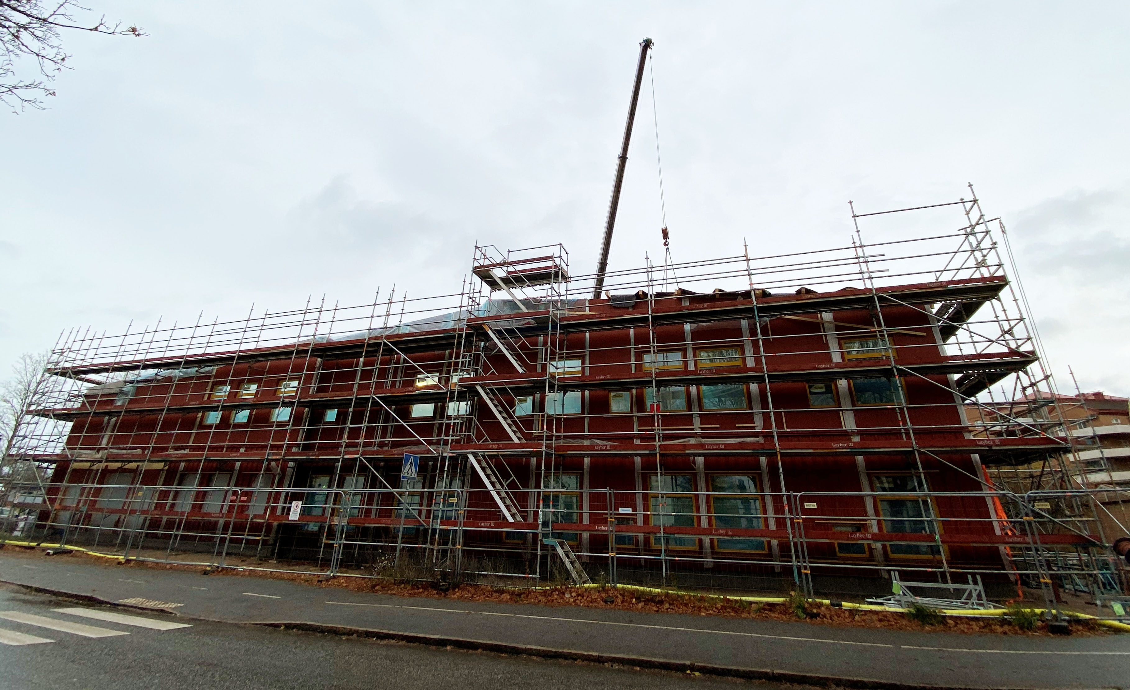 Byggplats för en ny, röd förskola med lyftkran i bakgrunden.