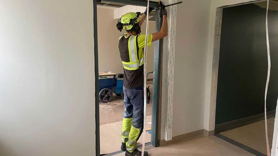 Invändig pågående renovering av skola där en man arbetar i en dörröppning.