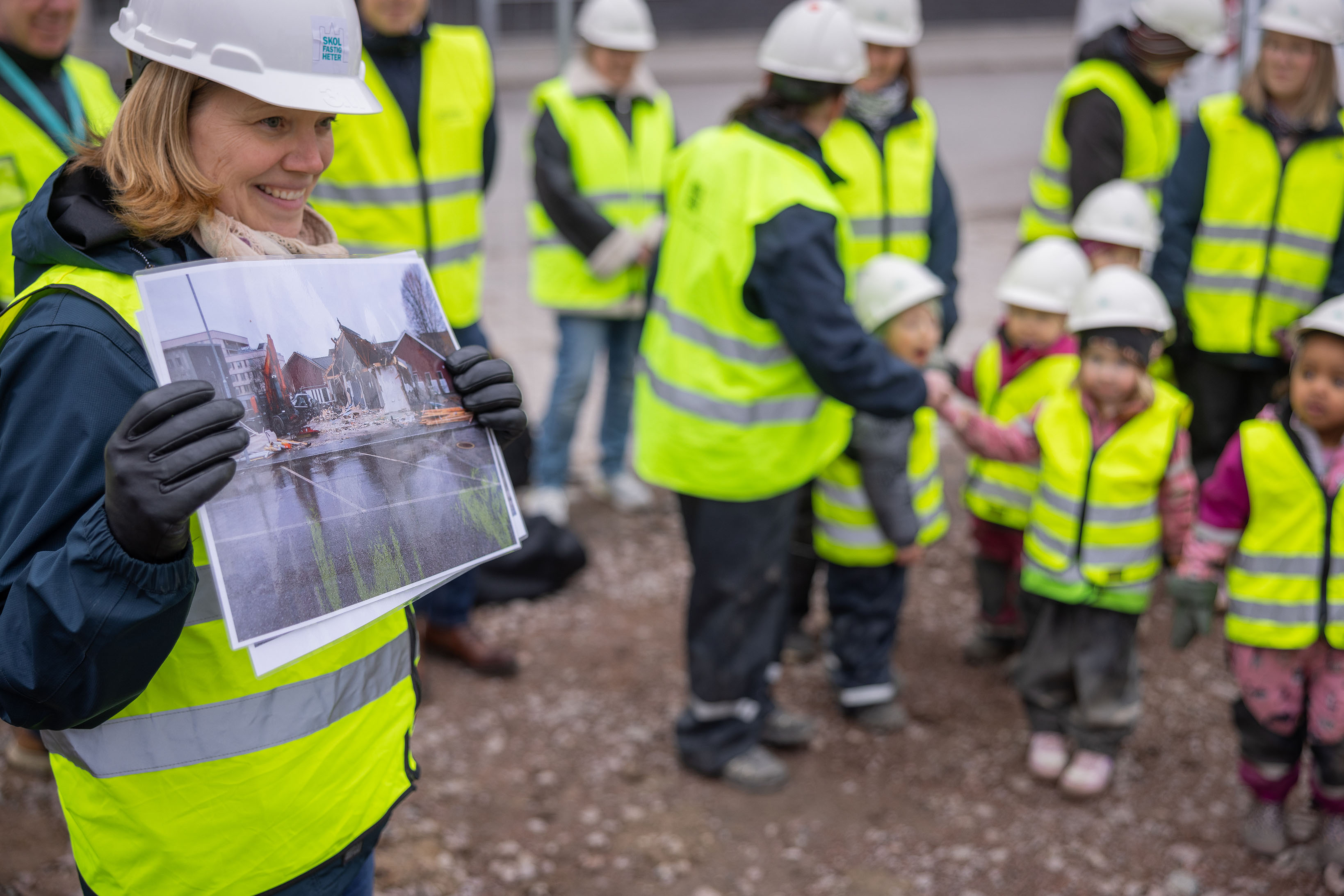 En kvinna med bygghjälm och väst visar upp ett foto.